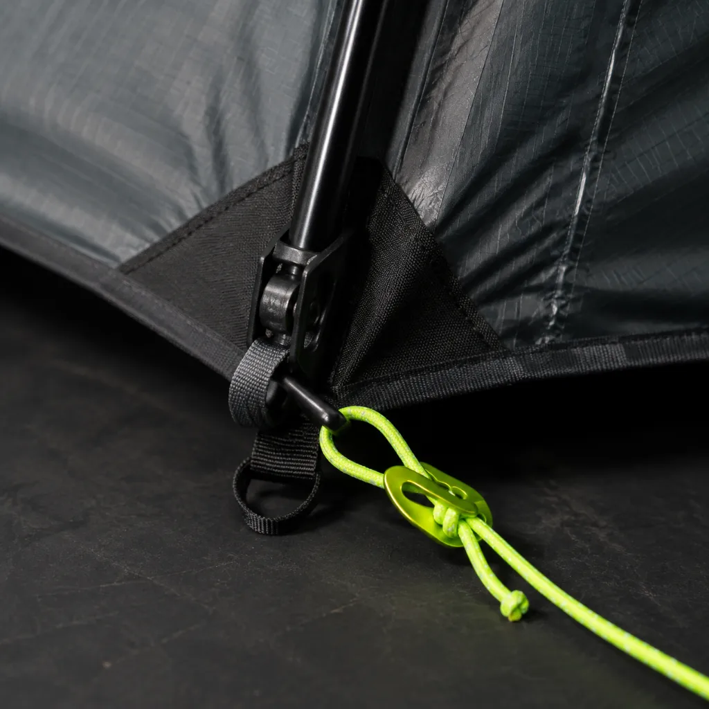 Macro view of graphite tent seam tape, pole clip, reinforced corner fabric, and acid-green guyline tensioner.