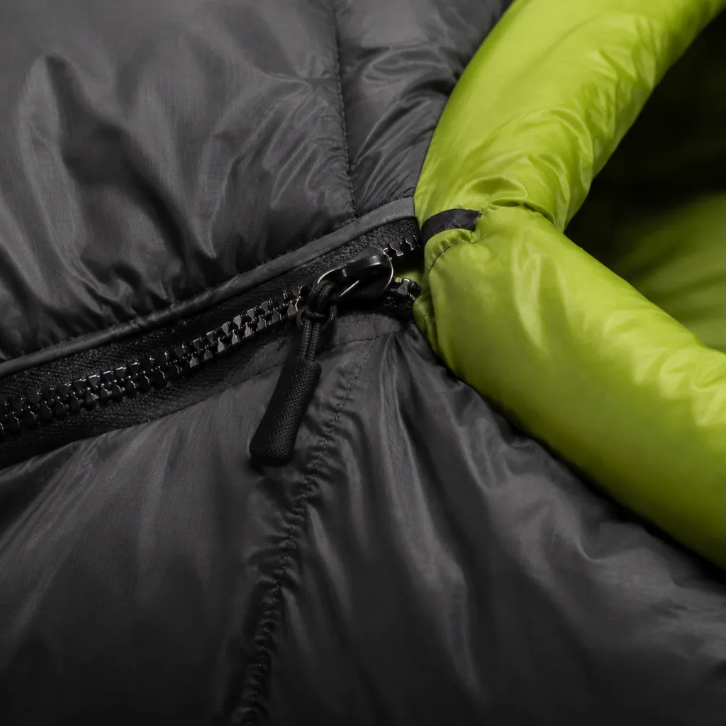 Close view of charcoal sleeping bag baffles, matte zipper teeth, pull tab, and acid-green draft fabric.